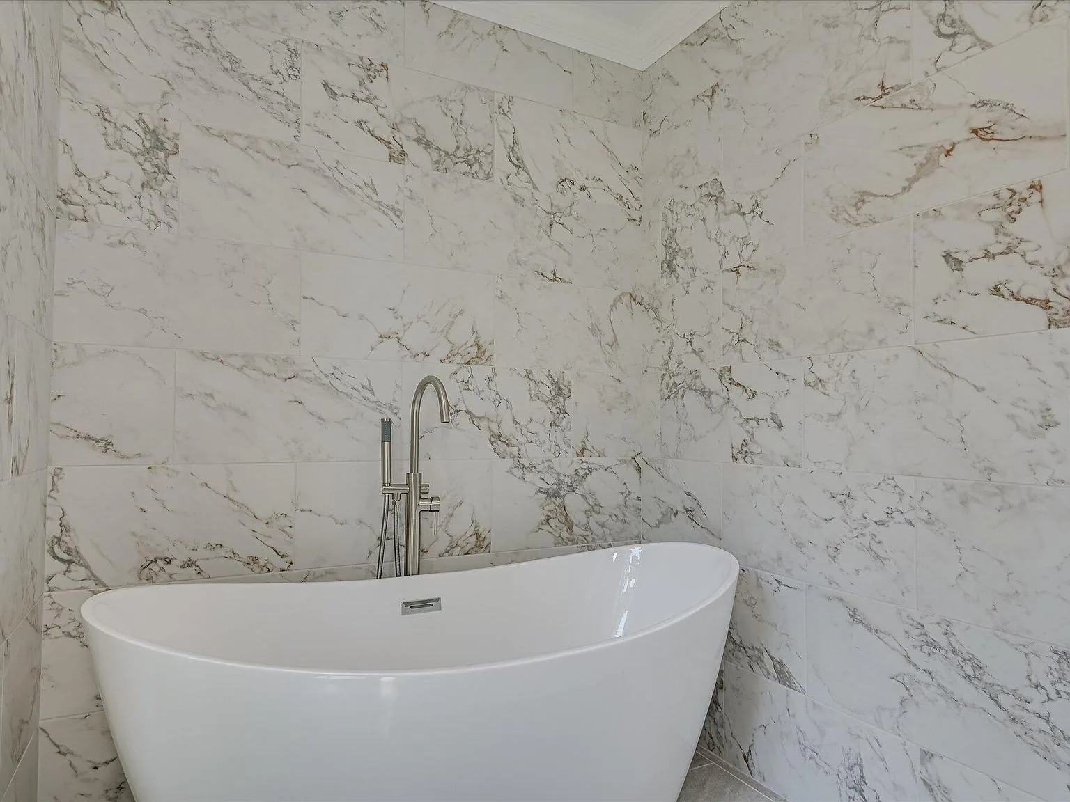 Primary bath freestanding soaking tub with marble-look tile at 4 Shadowmoor Court